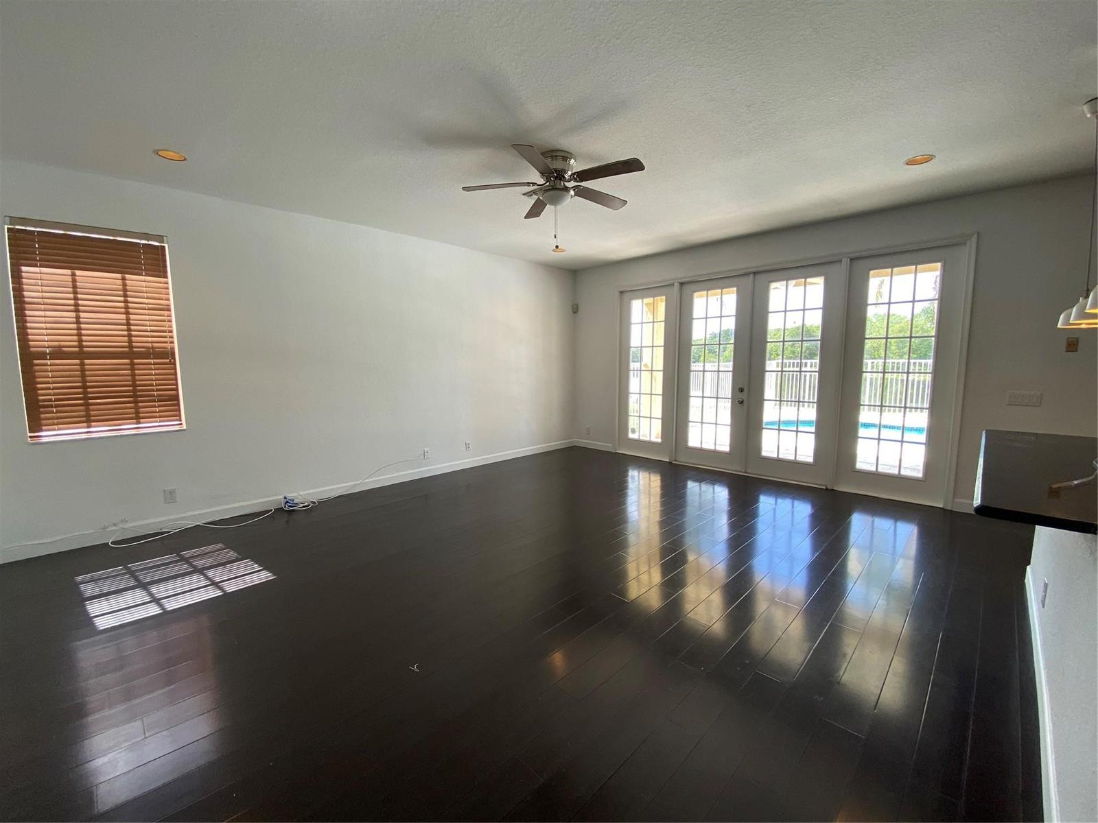 An empty living room features dark hardwood floors, a ceiling fan, and glass patio doors — 338 Cambridge Drive, Weston FL 33326, WESTON, FL