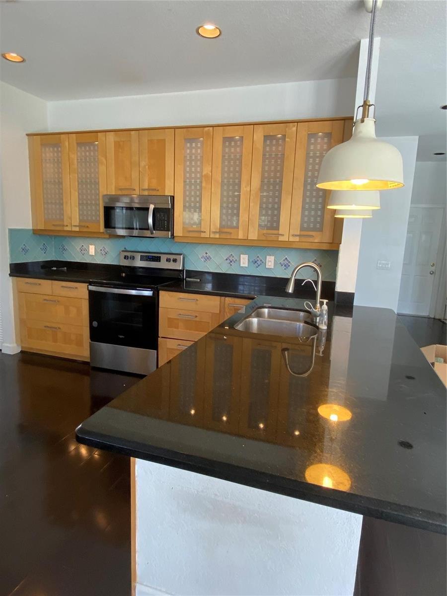 A kitchen features light wood cabinets, black countertops, a stainless steel stove, and pendant lighting — 338 Cambridge Drive, Weston FL 33326, WESTON, FL