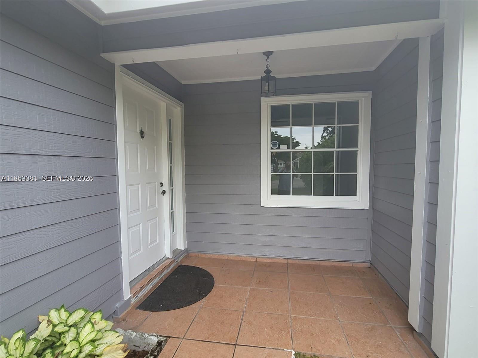 A covered entryway features gray horizontal siding, a white front door, and tiled flooring — 10304 SW 139th Pl, Miami FL 33186, MIAMI, FL