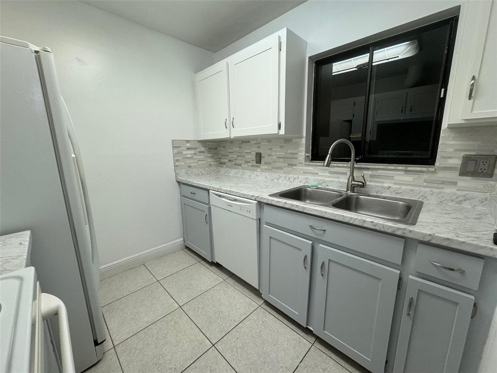 A kitchen features white upper cabinets, gray lower cabinets, a marble-look countertop, and tile flooring — 2304 INAGUA WAY UNIT 2304, WINTER PARK, FL