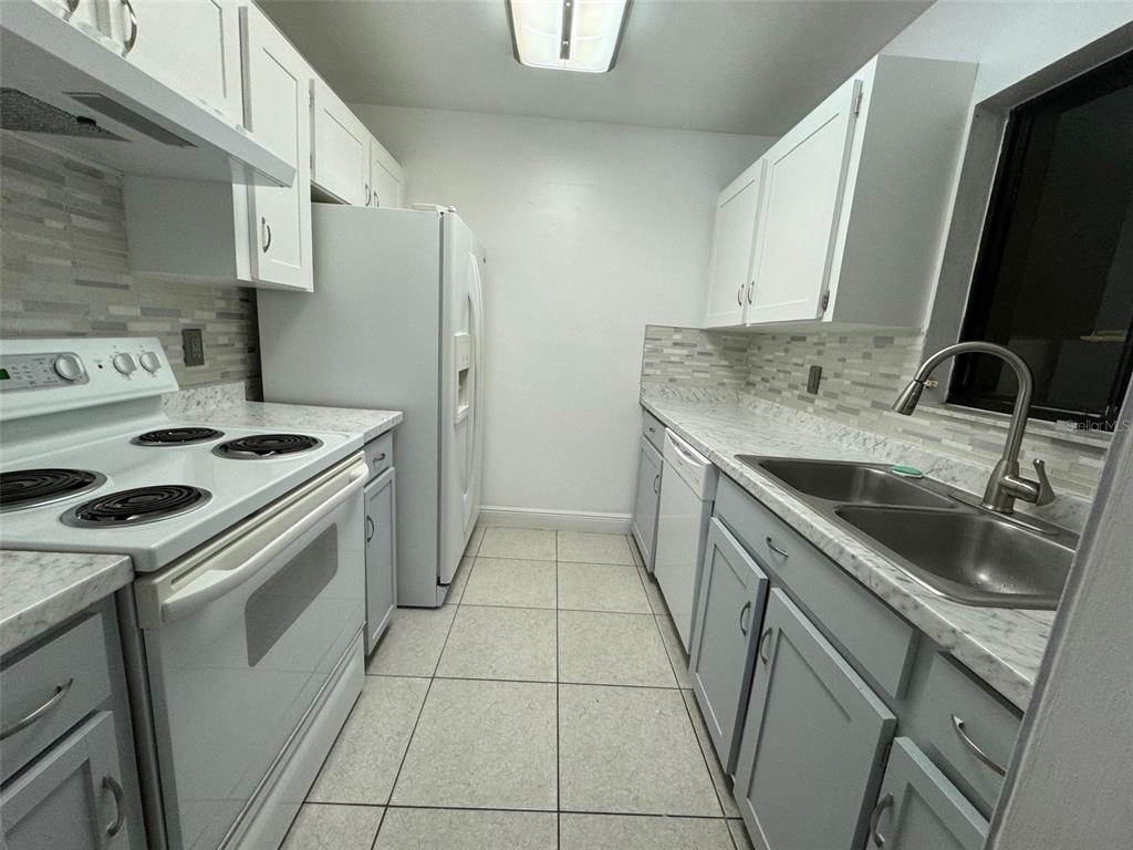 A galley kitchen features white cabinets, marble-look countertops, stainless steel sink, and white appliances — 2304 INAGUA WAY UNIT 2304, WINTER PARK, FL