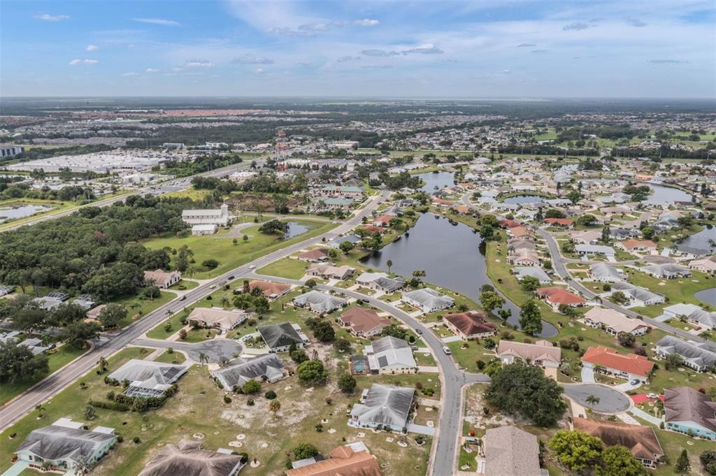 An aerial view shows a suburban neighborhood with houses, a lake, and a nearby road — 1209 WILD FEATHER LANE, SUN CITY CENTER, FL