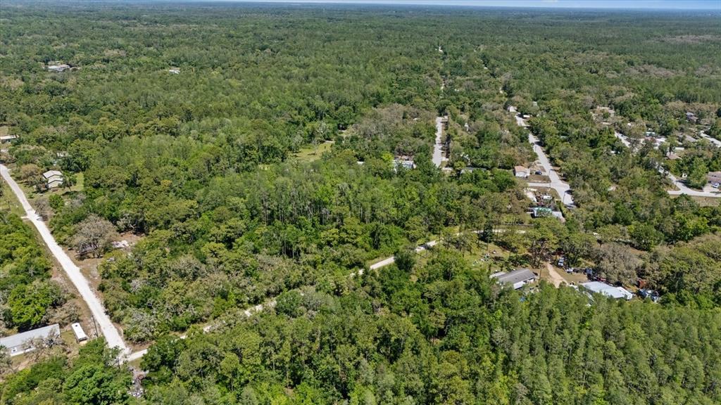 An aerial view shows a wooded residential area with dirt roads and scattered houses — 12914 MIDVALE AVENUE, NEW PORT RICHEY, FL