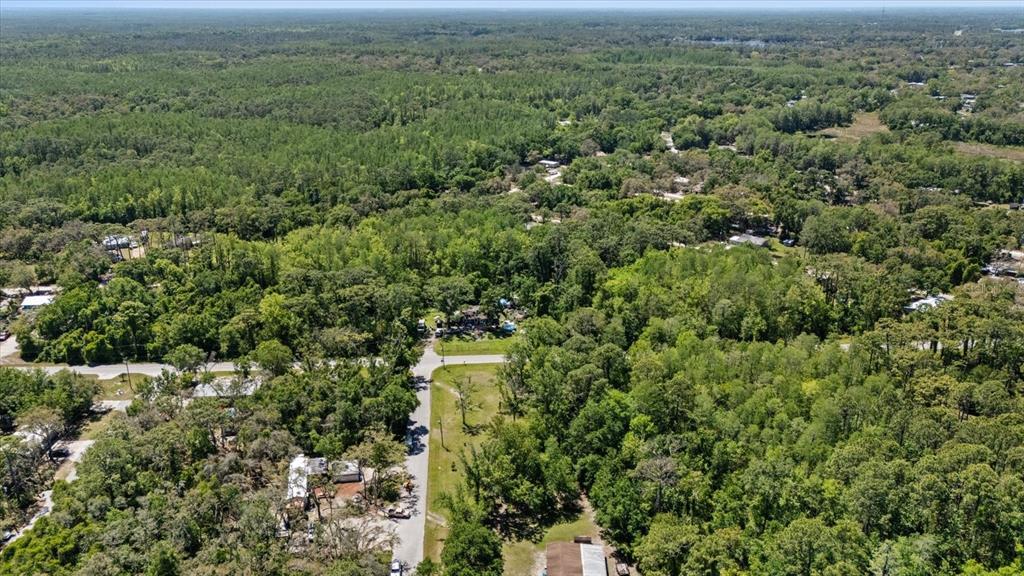 An aerial view shows a wooded residential area with scattered houses and a paved road — 12914 MIDVALE AVENUE, NEW PORT RICHEY, FL