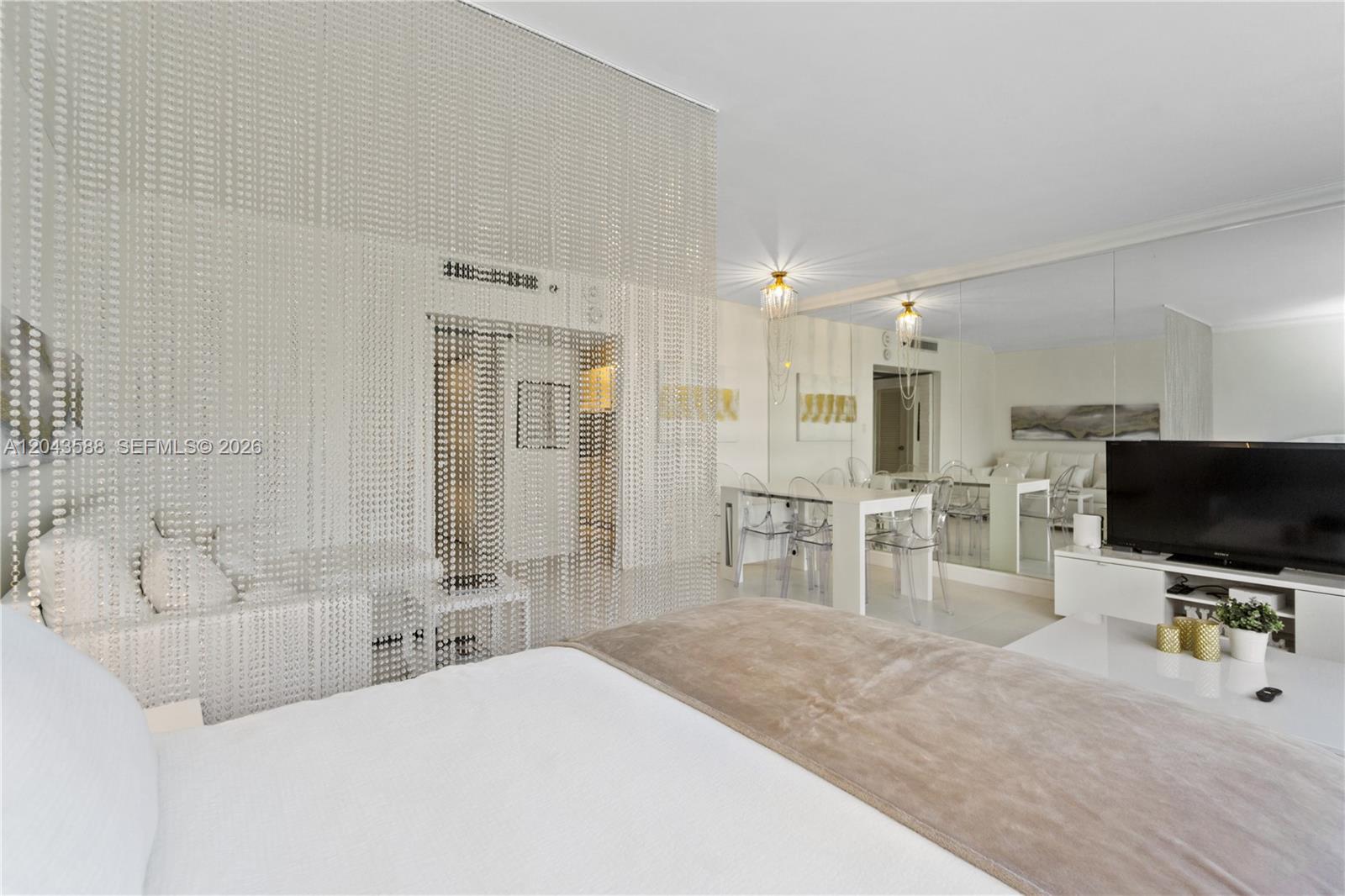 A bedroom features a beaded curtain room divider, a white bed, and mirrored walls — 100 Lincoln Rd # 306, Miami Beach FL 33139, MIAMI BEACH, FL