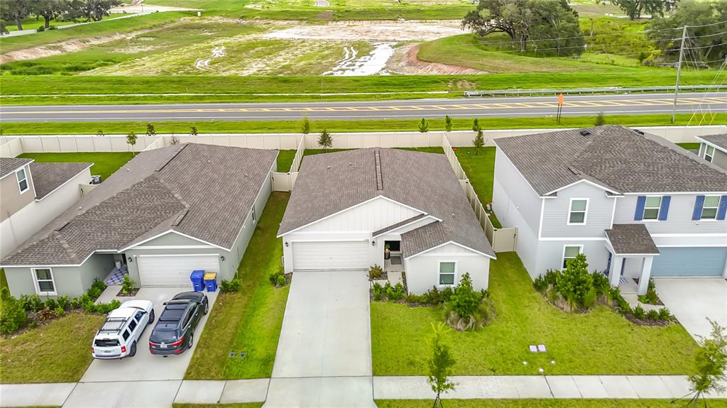 An aerial view shows three suburban houses with driveways and lawns near a road and field — 11938 BRAE, DADE CITY, FL