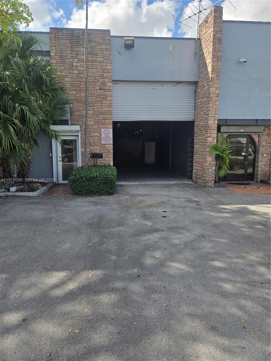 The exterior of a commercial building features a roll-up warehouse door, stone accents, and landscaping — 7480 NW 52nd St, Miami FL 33166, MIAMI, FL