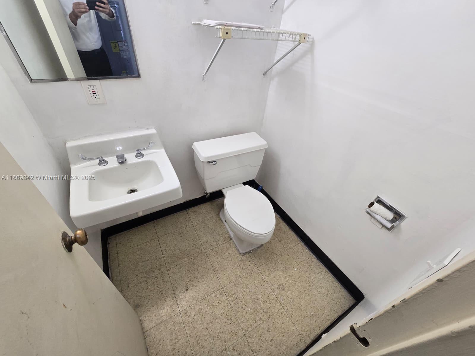 A small bathroom features a wall-mounted sink, a white toilet, and a wire storage shelf — 2501 N State Road 7 # 2533, Margate FL 33063, MARGATE, FL