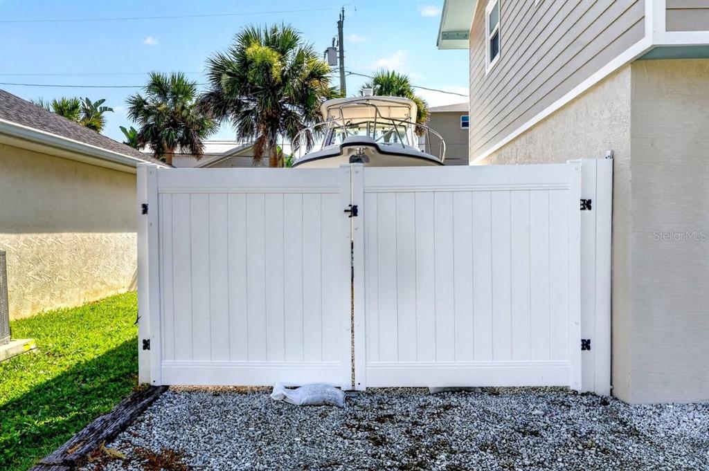A white vinyl double gate stands between a house and a side yard with gravel — 4717 S ATLANTIC AVENUE, NEW SMYRNA BEACH, FL