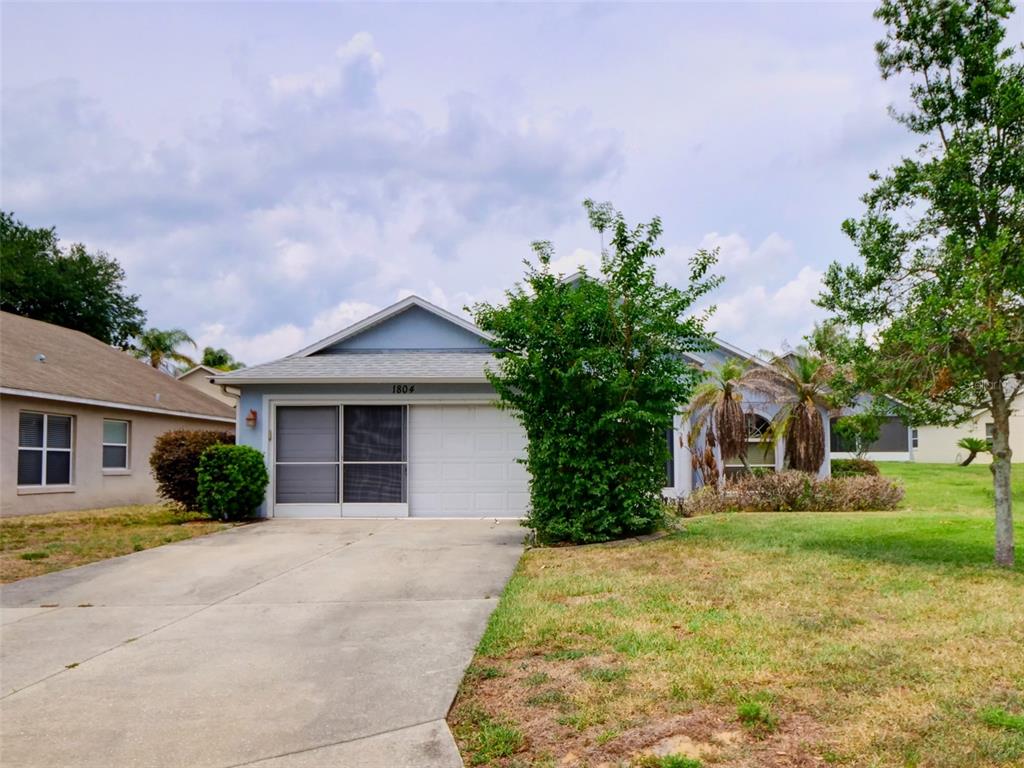 A single-story house with a white garage, a driveway, and a large bush in front — 1804 LAKE VILLA DRIVE, TAVARES, FL