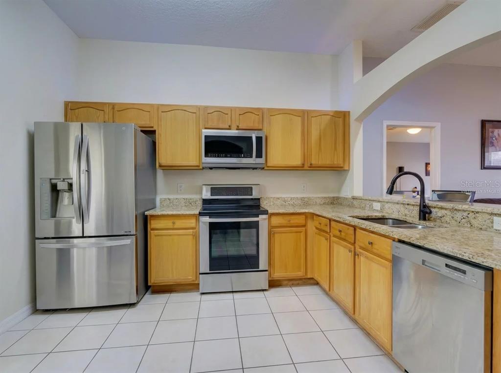A kitchen with oak cabinets, granite countertops, stainless steel appliances, and white tile flooring — 1804 LAKE VILLA DRIVE, TAVARES, FL