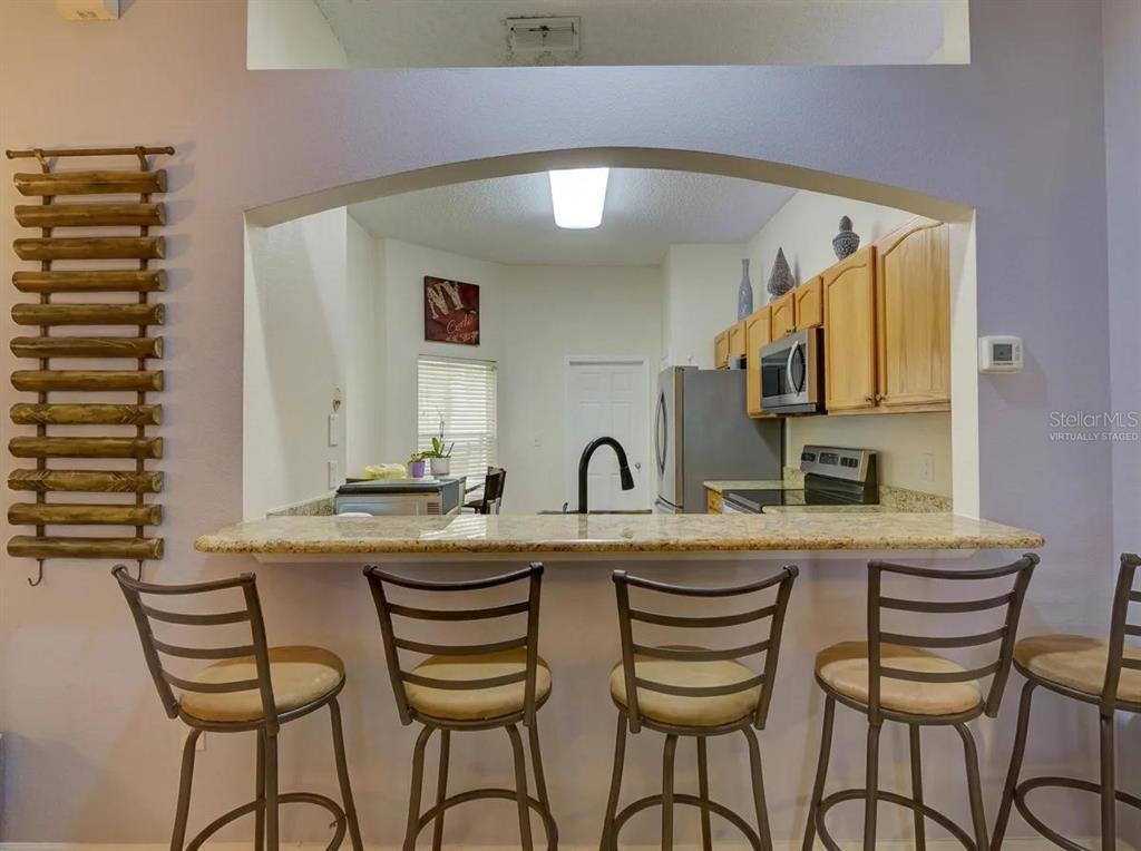 A kitchen with wooden cabinets and a granite breakfast bar featuring four metal stools — 1804 LAKE VILLA DRIVE, TAVARES, FL