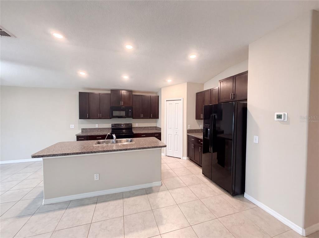 A kitchen features dark wood cabinets, granite countertops, a center island, and black appliances — 39693 HARVEST CREEK LANE, ZEPHYRHILLS, FL