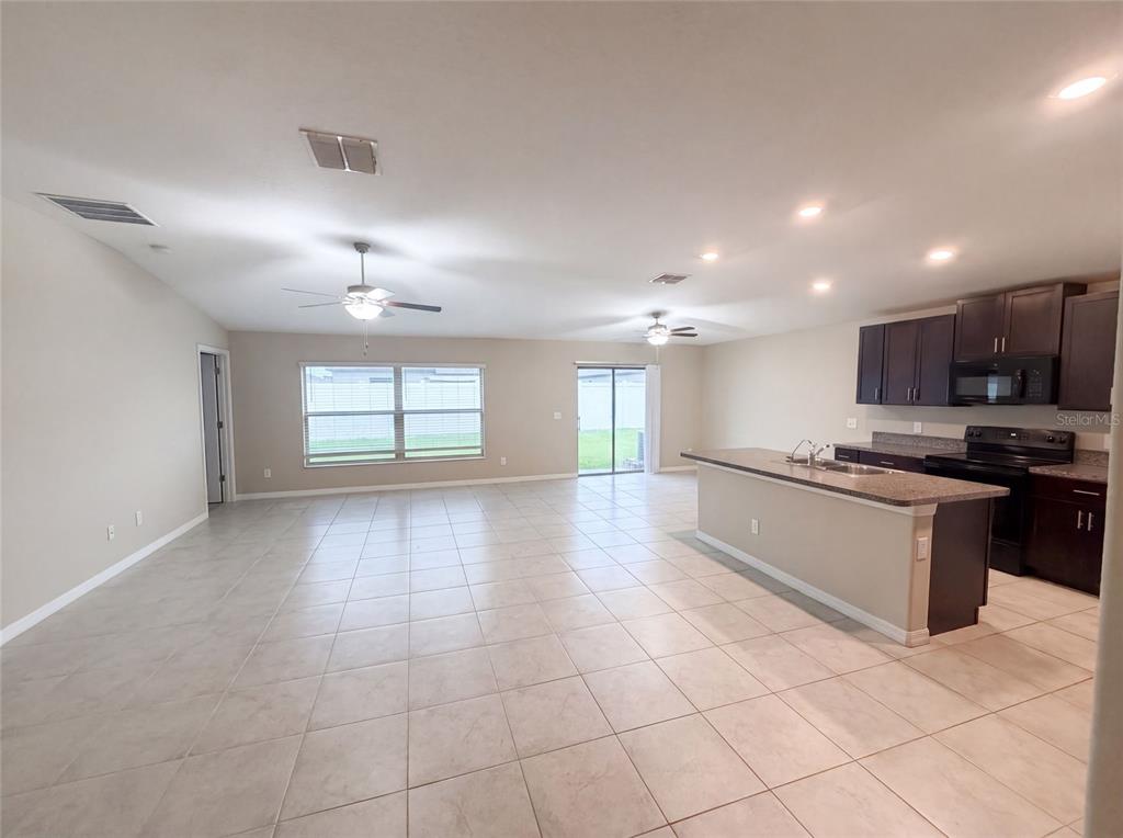 An open-concept living and kitchen area features tile flooring, dark cabinetry, and a center island — 39693 HARVEST CREEK LANE, ZEPHYRHILLS, FL