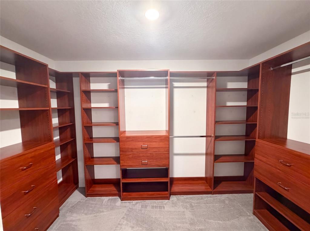 A walk-in closet features custom cherry-toned wooden shelving, hanging rods, and built-in drawer units — 39693 HARVEST CREEK LANE, ZEPHYRHILLS, FL