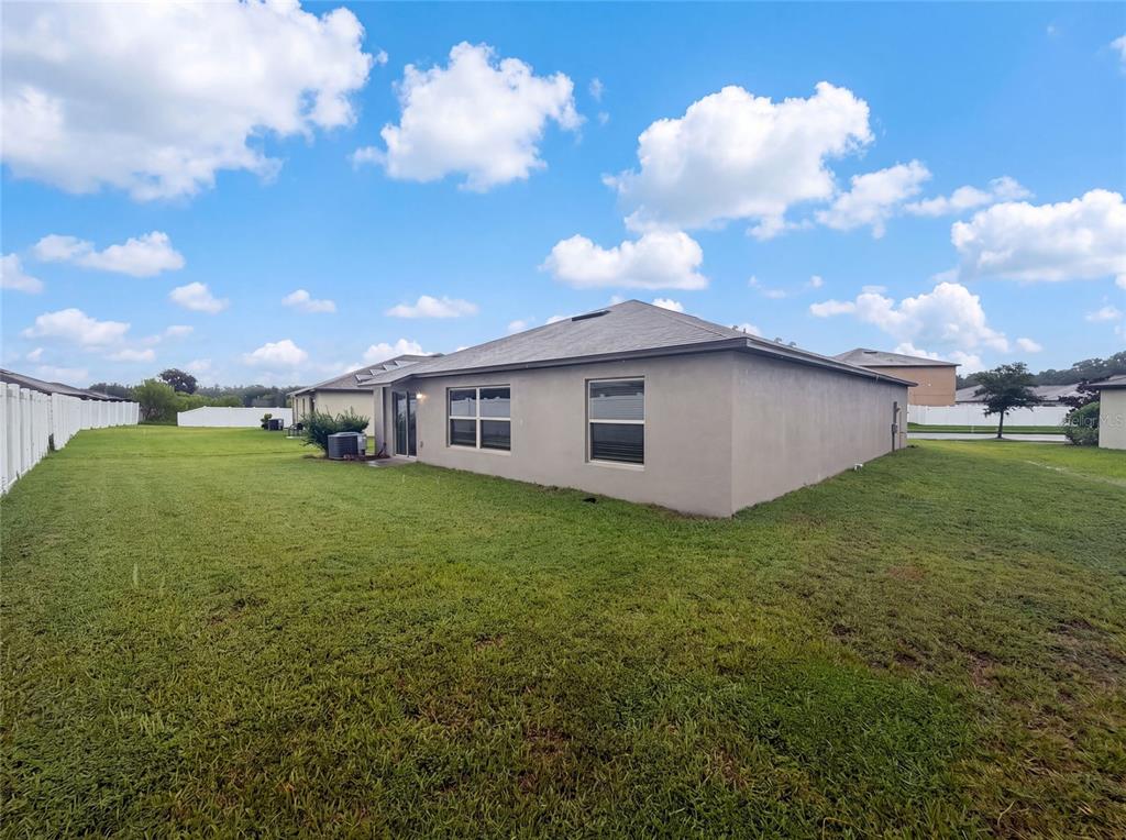 The exterior rear view of a single-story house features a tan stucco wall and lawn — 39693 HARVEST CREEK LANE, ZEPHYRHILLS, FL