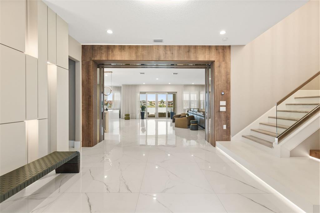 A modern foyer features white marble floors, a floating staircase, and a wood-paneled entryway — 15499 SHOREBIRD LANE, WINTER GARDEN, FL
