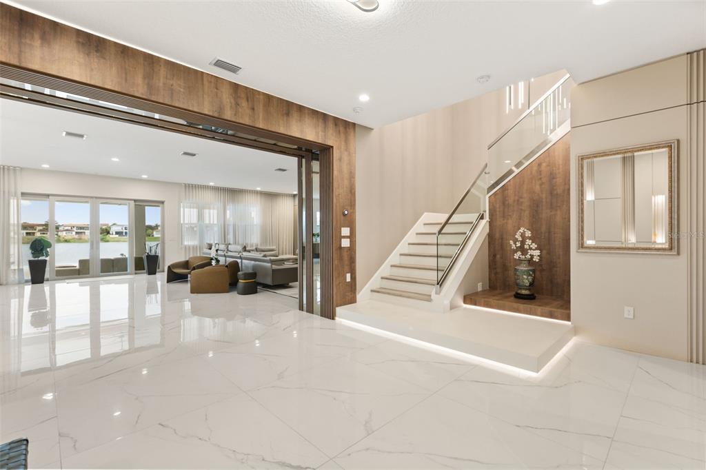A modern foyer features white marble floors, a floating staircase, and a view into a living room — 15499 SHOREBIRD LANE, WINTER GARDEN, FL