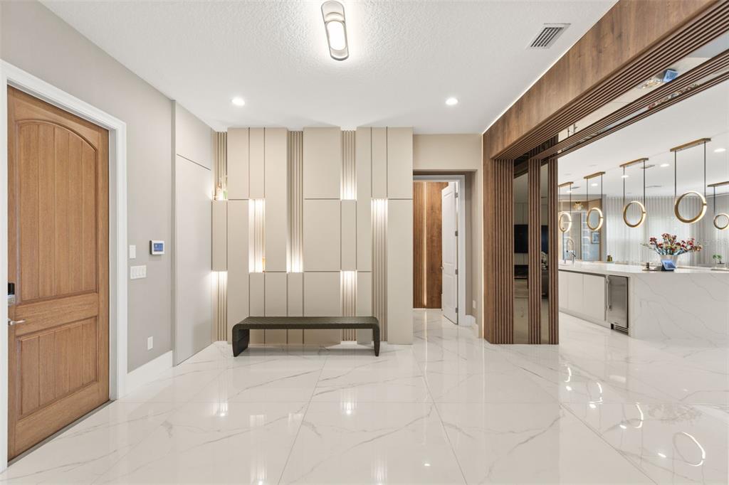 A modern entryway features white marble floors, a paneled accent wall with integrated lighting, and wood-trimmed doorways — 15499 SHOREBIRD LANE, WINTER GARDEN, FL