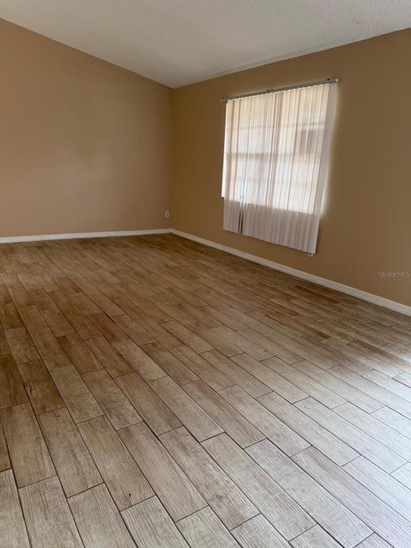 An empty room features light brown wood-look tile flooring, tan walls, and a window with blinds — 1726 MONTICELLO STREET, DELTONA, FL
