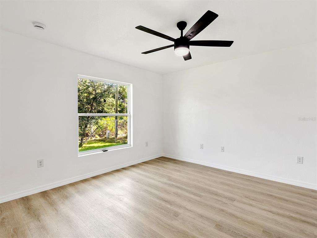 An empty bedroom features white walls, light wood-look flooring, a ceiling fan, and one window — 12168 GROSSPOINT AVENUE, PORT CHARLOTTE, FL