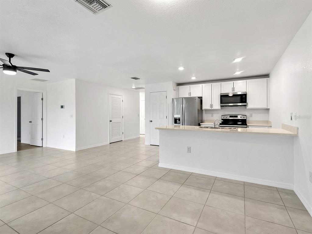 A kitchen with white cabinets and stainless steel appliances overlooks a tiled living area — 12168 GROSSPOINT AVENUE, PORT CHARLOTTE, FL