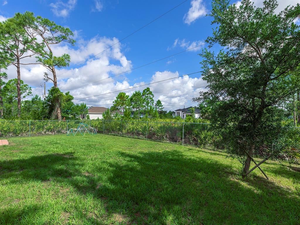 A grassy backyard features a chain-link fence, a small climbing dome, and surrounding trees — 12168 GROSSPOINT AVENUE, PORT CHARLOTTE, FL
