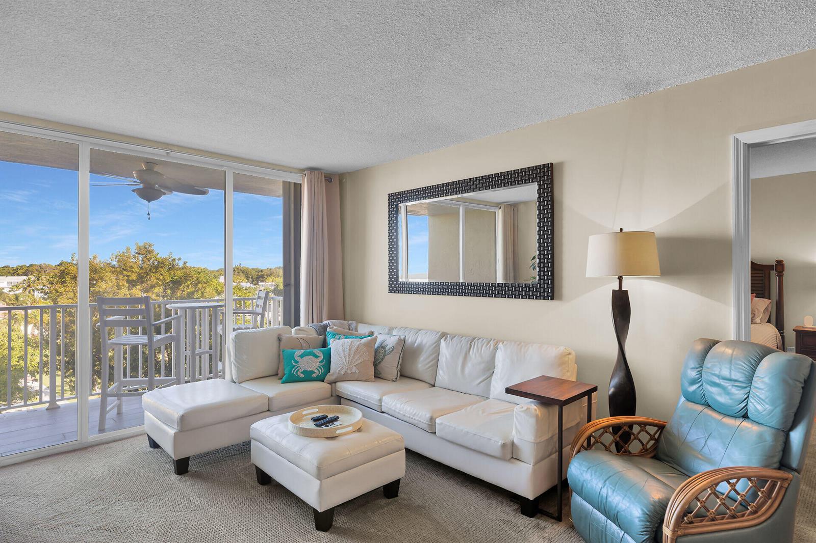 A living room features a white sectional sofa, a blue armchair, and a balcony view — 88540 Overseas Highway # 304, Tavernier FL 33070, TAVERNIER, FL