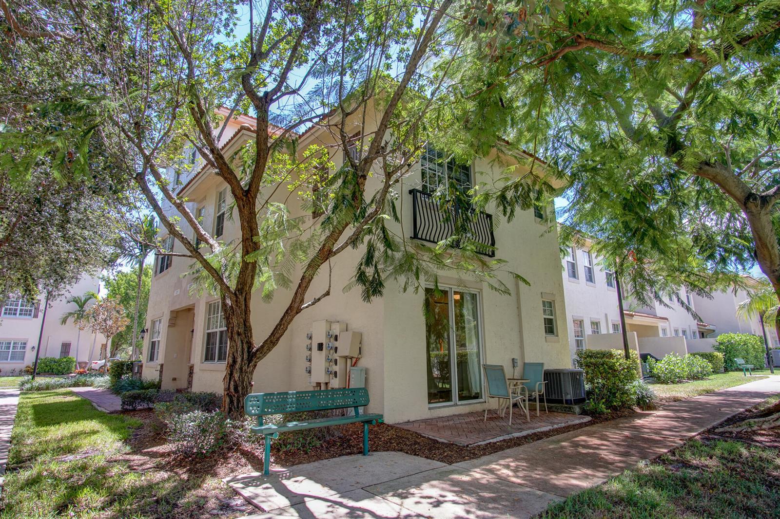Exterior view of a multi-story residential building with a patio, green bench, and mature trees — 1020 E Longport Circle # F2, Delray Beach FL 33444, DELRAY BEACH, FL