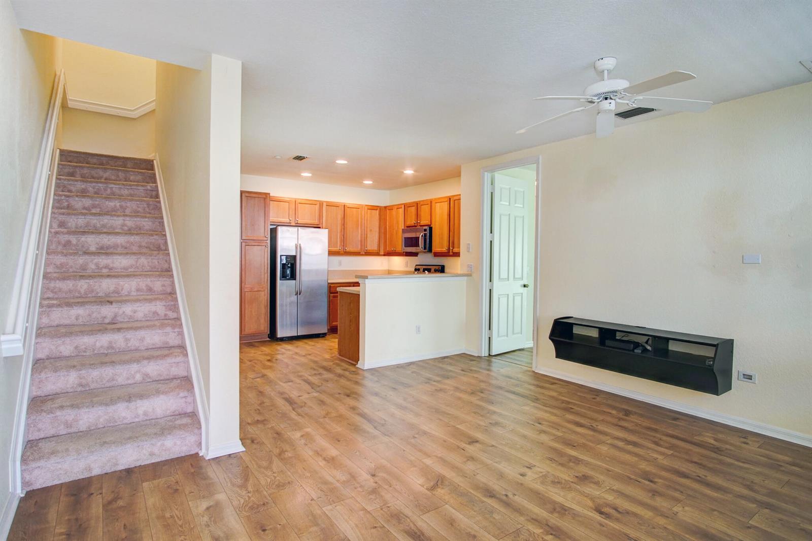 An open-concept living area features wood-look flooring, a kitchen with wood cabinets, and carpeted stairs — 1020 E Longport Circle # F2, Delray Beach FL 33444, DELRAY BEACH, FL