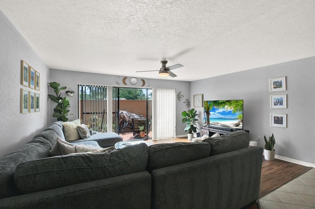 A living room features a large gray sectional sofa, a television, and a sliding glass door — 6100 GULFPORT BOULEVARD S UNIT 111, GULFPORT, FL