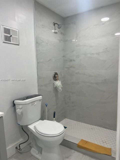 A bathroom features a white toilet next to a walk-in shower with gray tiled walls — MIAMI, FL