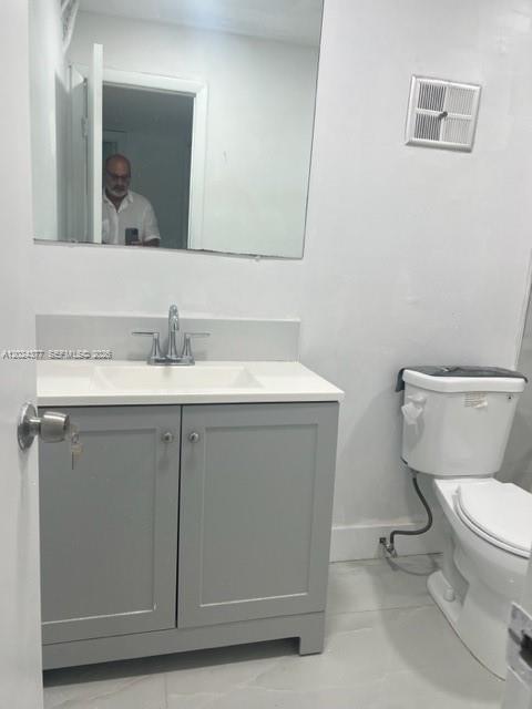 A bathroom features a grey vanity with a white countertop, a mirror, and a toilet — MIAMI, FL