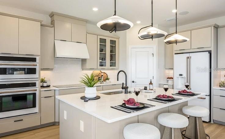 A modern kitchen features light-colored cabinetry, a large central island with seating, and pendant lighting — 7717 BLUE MOON RUN, SARASOTA, FL