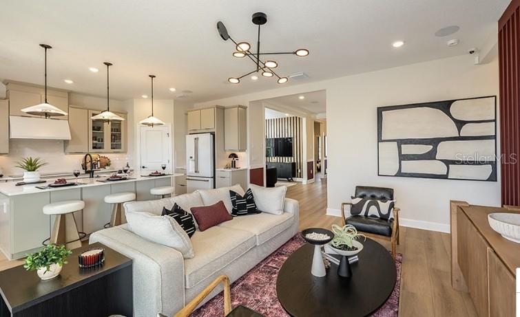 An open-concept living room and kitchen feature a light sofa, modern lighting, and wood flooring — 7717 BLUE MOON RUN, SARASOTA, FL