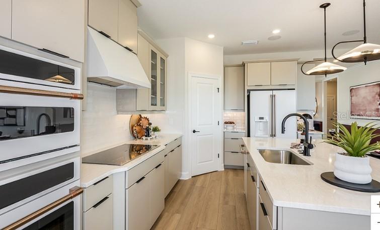A modern kitchen features light-colored cabinetry, a large island with a sink, and stainless appliances — 7717 BLUE MOON RUN, SARASOTA, FL