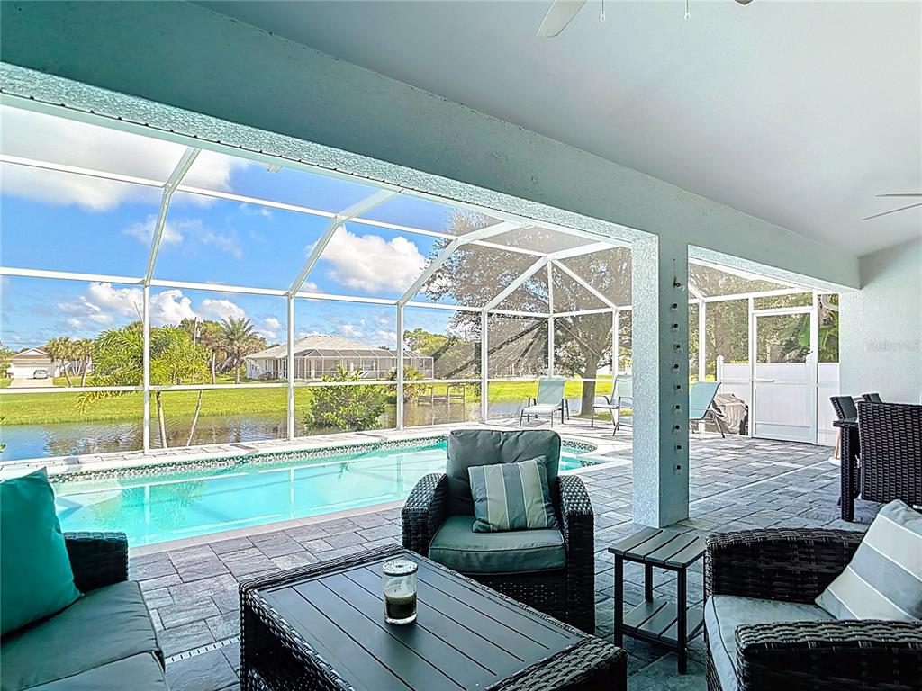 A covered patio features a swimming pool, wicker furniture, and a screened-in enclosure — 202 LONG MEADOW LANE, ROTONDA WEST, FL