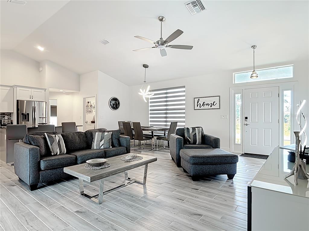 An open-concept living and dining area features gray tile flooring, a dark sofa, and white walls — 202 LONG MEADOW LANE, ROTONDA WEST, FL