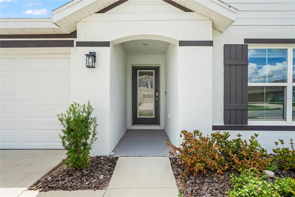 The exterior of a house features a white stucco facade, a dark front door, and shutters — 4041 AUTUMN AMBER, SPRING HILL, FL