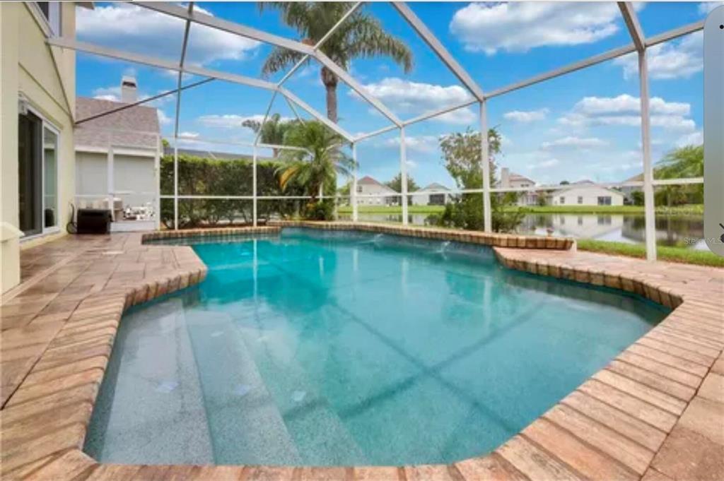 A screened-in swimming pool with a brick paver deck overlooks a lake and neighboring houses — 624 HARDWOOD CIRCLE, ORLANDO, FL