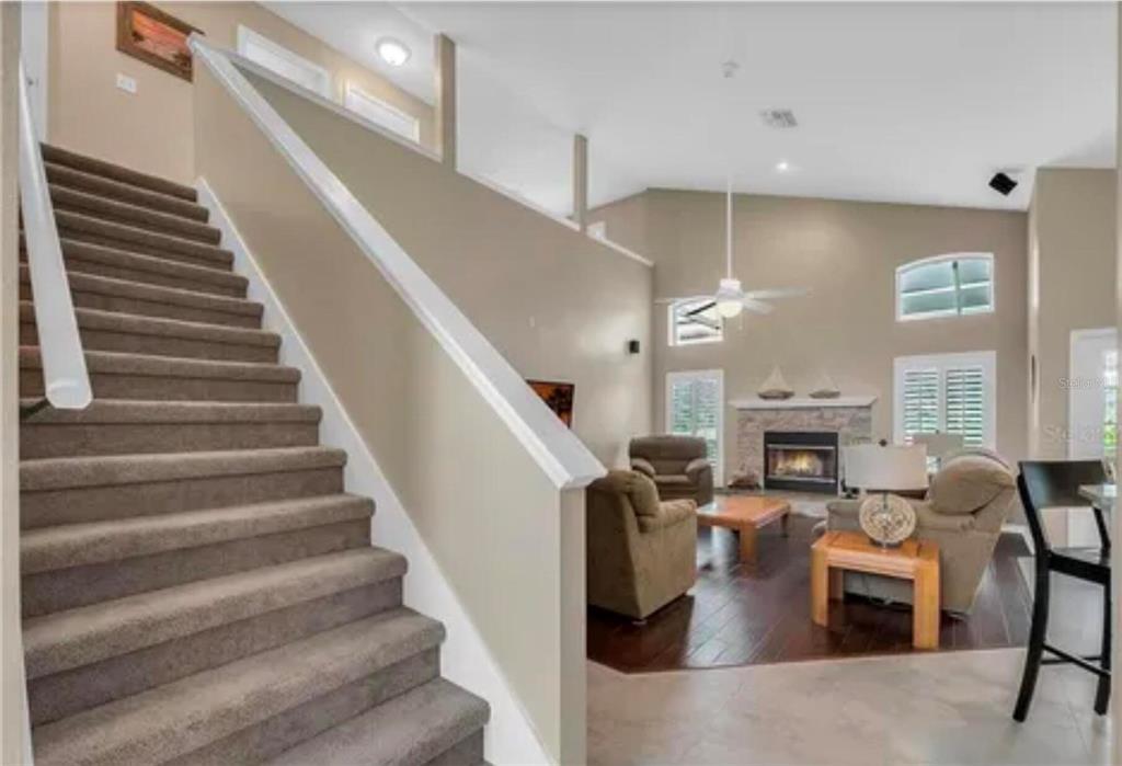 A staircase with carpeted steps leads down to a living room with a stone fireplace — 624 HARDWOOD CIRCLE, ORLANDO, FL