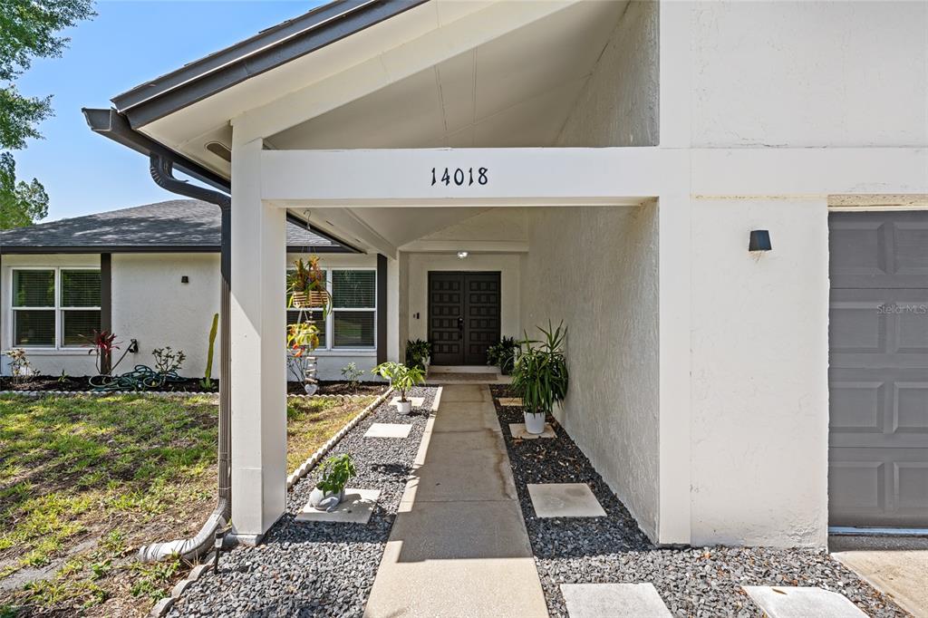 A concrete walkway leads to the dark double front doors of a white house — 14018 CASCADE LANE, TAMPA, FL