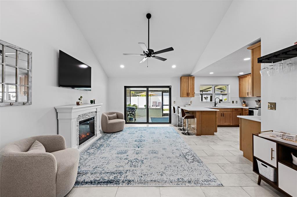 An open-concept living room and kitchen featuring a fireplace, area rug, and sliding glass doors — 14018 CASCADE LANE, TAMPA, FL