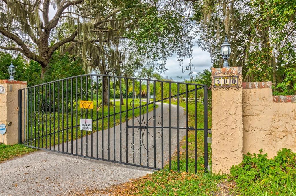 A black metal gate stands between two stucco pillars at the entrance to a driveway — 500 N HIGHLAND AVENUE, TARPON SPRINGS, FL