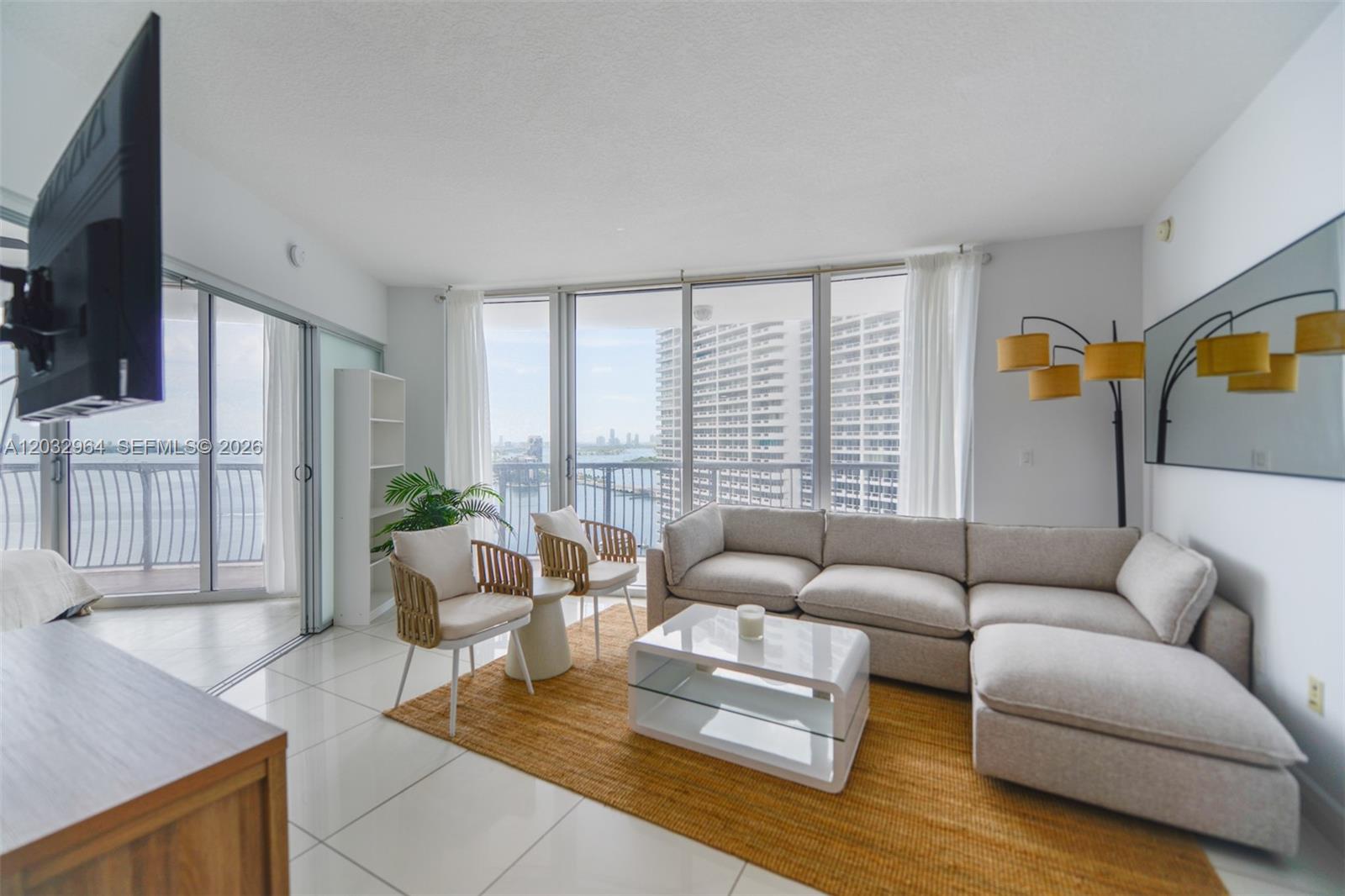 A living room features a sectional sofa, white tile floors, and floor-to-ceiling windows with water views — 1750 N Bayshore Dr # 2402, Miami FL 33132, MIAMI, FL