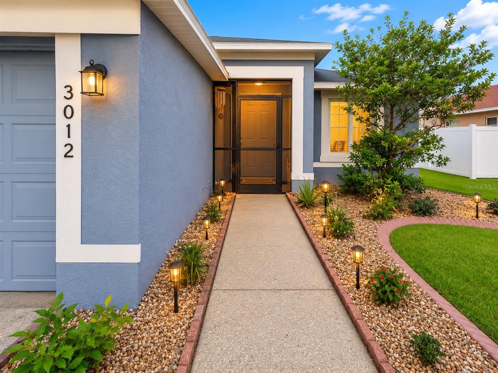 A blue house exterior features a concrete walkway, landscaping, and a screened front entryway — 3012 SUMMER HOUSE DRIVE, VALRICO, FL
