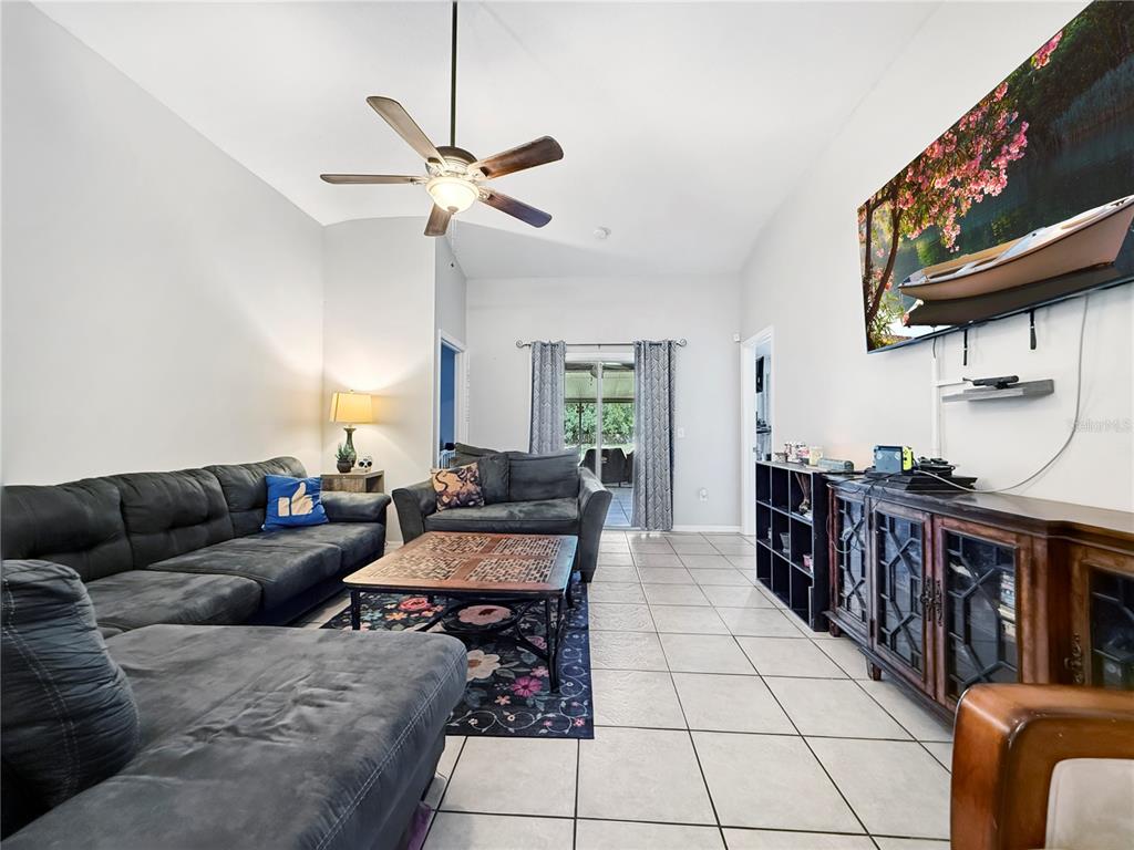 A living room features gray sectional sofas, a patterned rug, tile flooring, and a television — 3012 SUMMER HOUSE DRIVE, VALRICO, FL