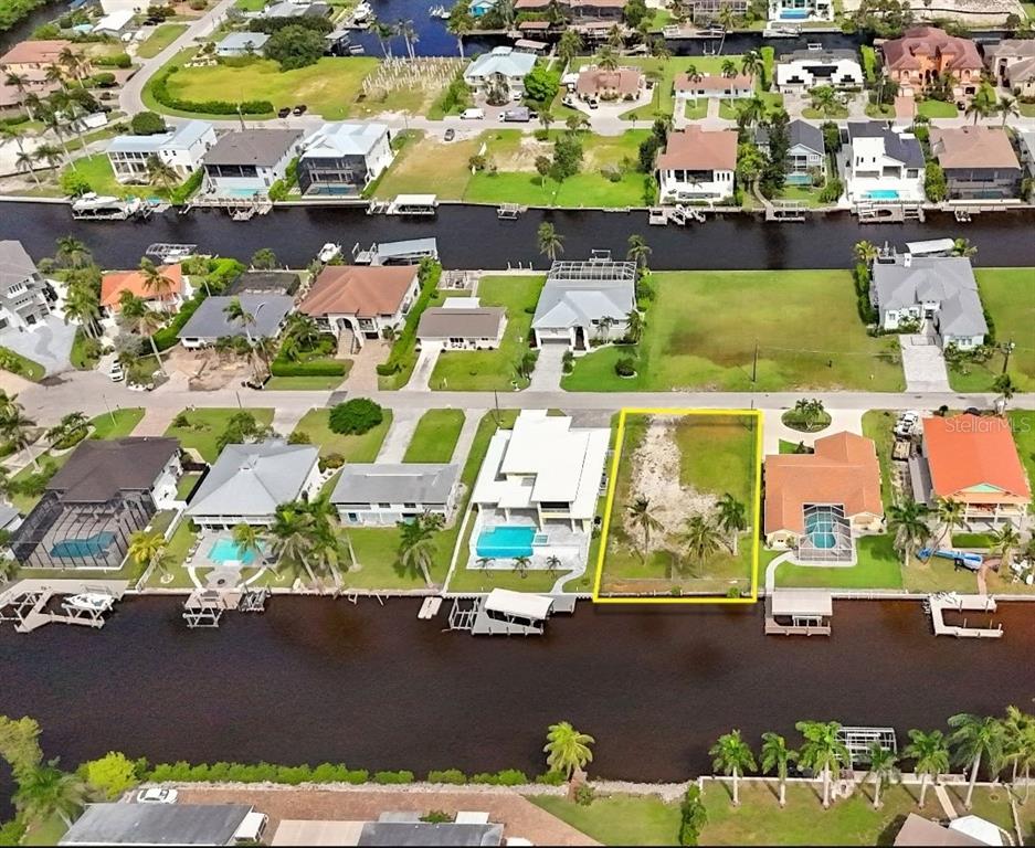 An aerial view shows a vacant waterfront lot outlined in yellow between two residential houses — 4851 & 4853 REGAL DR, BONITA SPRINGS, FL