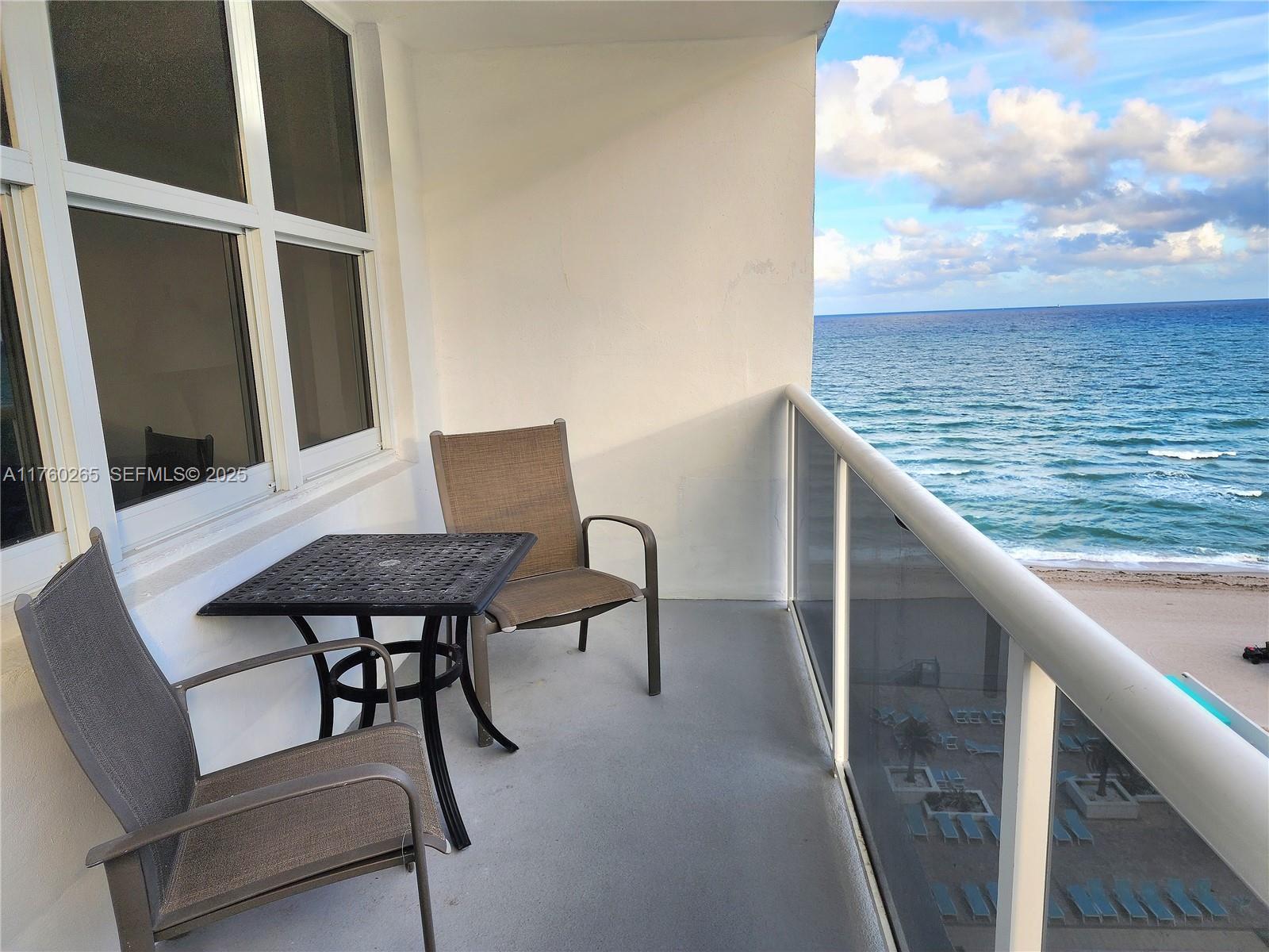 A balcony with a small table and two chairs overlooks the ocean and beach — 3725 S Ocean Dr # 1008, Hollywood FL 33019, HOLLYWOOD, FL