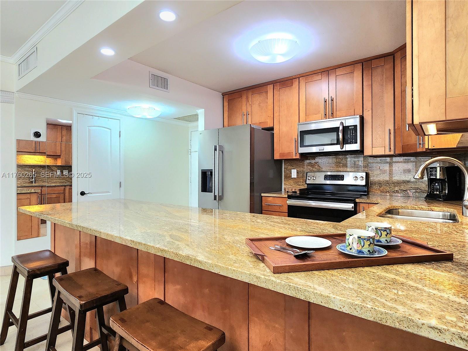 A kitchen features wood cabinets, granite countertops, a breakfast bar with stools, and stainless appliances — 3725 S Ocean Dr # 1008, Hollywood FL 33019, HOLLYWOOD, FL